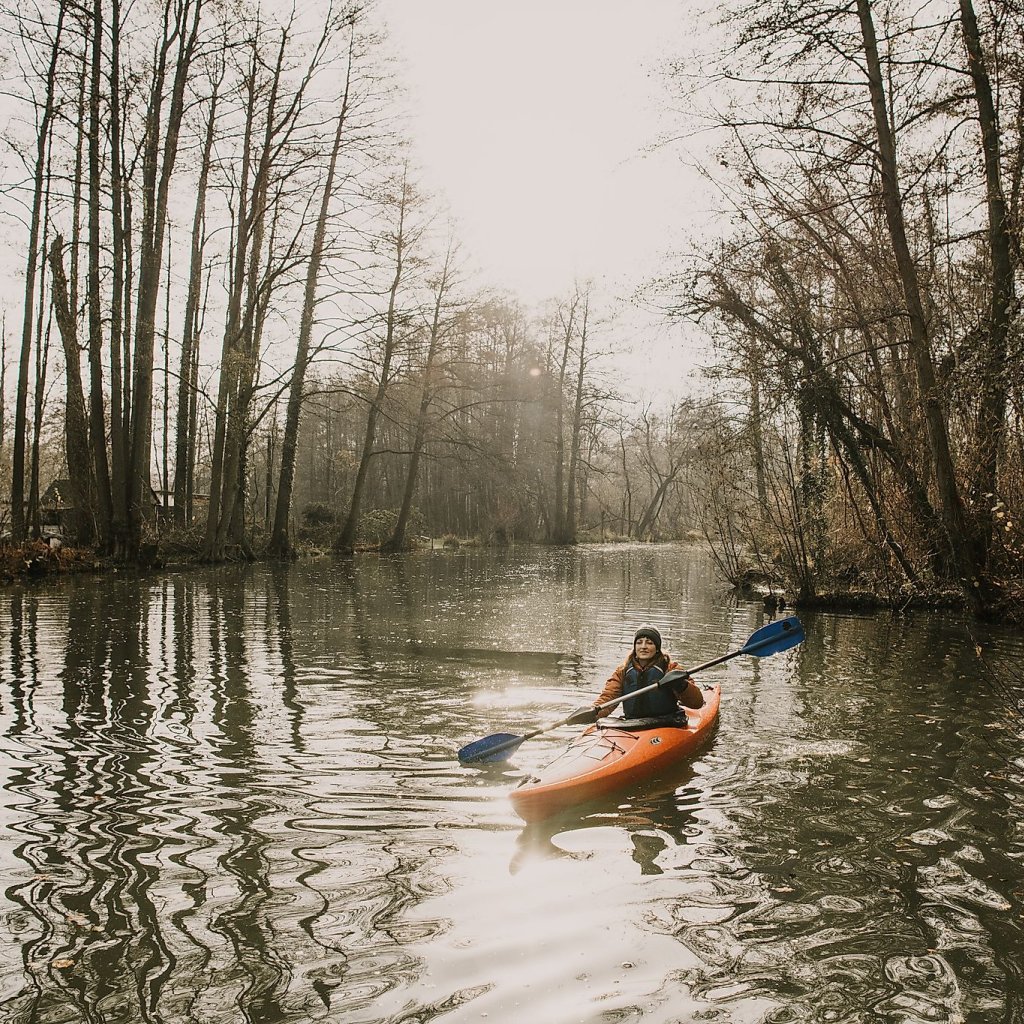 Person in einem Kanu vor winterlicher Landschaft und kahlen Bäumen